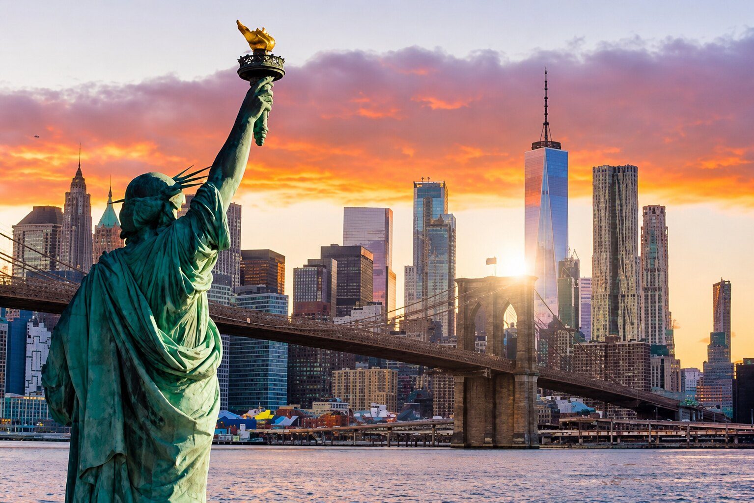 The Statue of Liberty overlooking the Brooklyn Bridge and Lower Manhattan at sunset