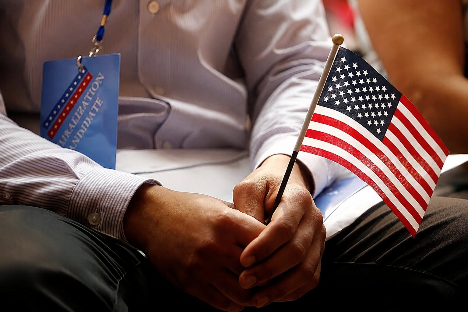 An immigration candidate holding a small American flag while waiting at a ceremony