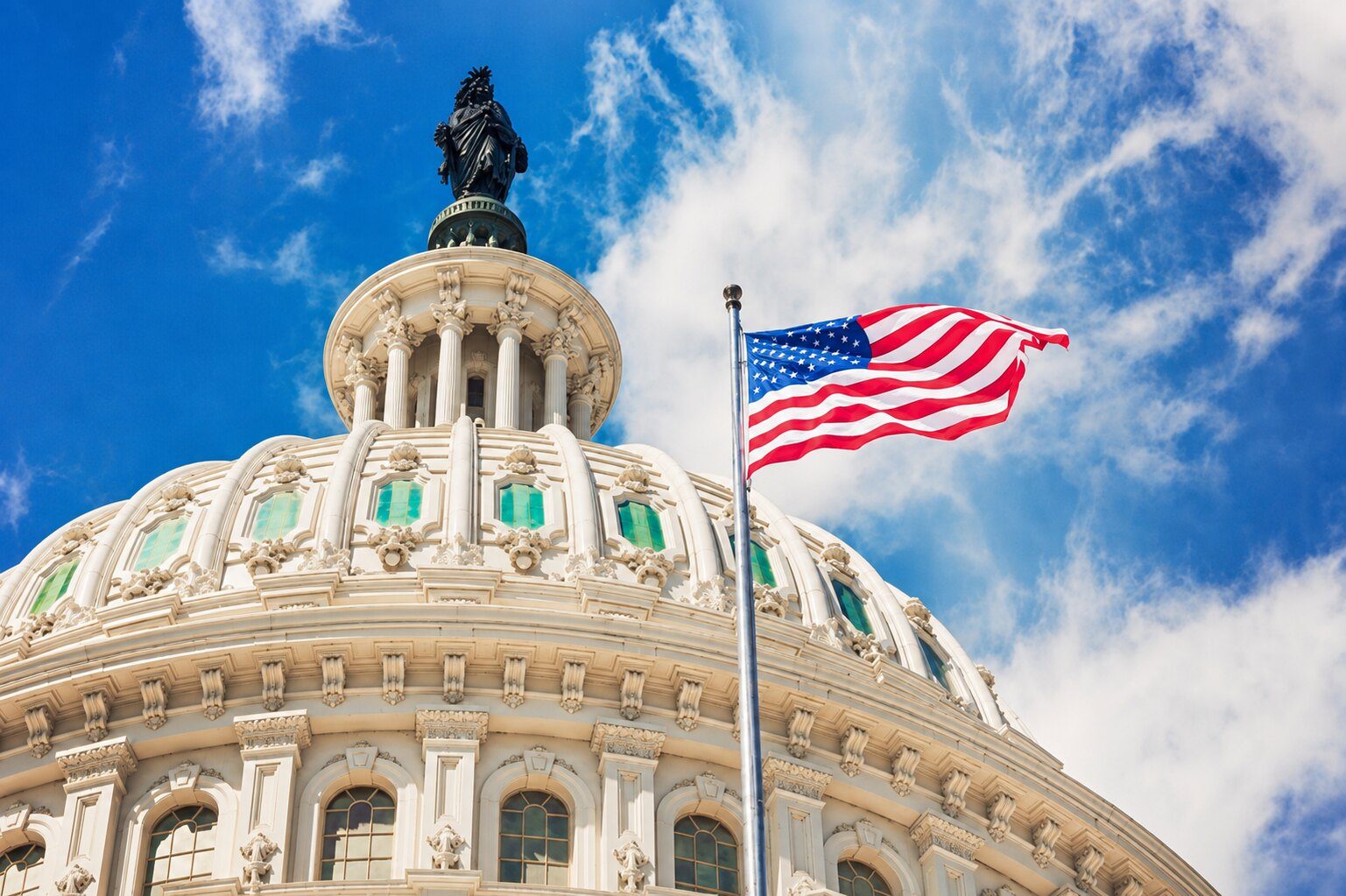 The United States Capitol dome beside an American flag under a bright blue sky