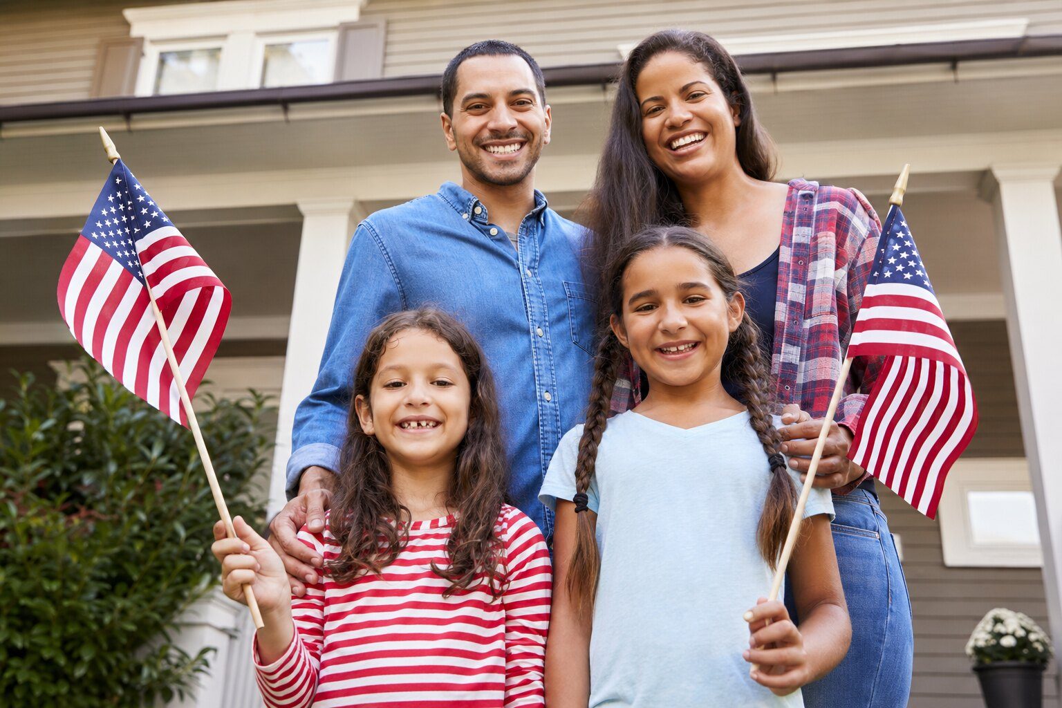 A family of four holding American flags outside their home