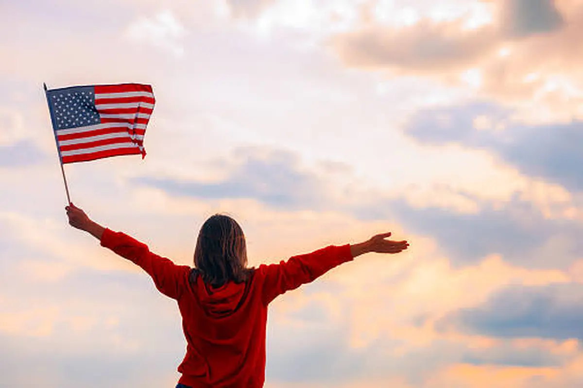 Person holding a small American flag against a cloudy sky
